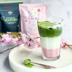 a drink with green and pink in it on a white plate next to some flowers