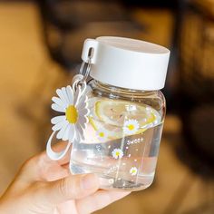 a person holding a glass jar with lemon slices and daisies on it, while wearing a daisy keychain