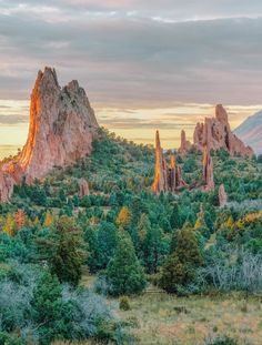 the sun is setting over some rocks and trees in front of a mountain range with tall rock formations