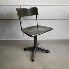 a black office chair sitting on top of a cement floor next to a white wall