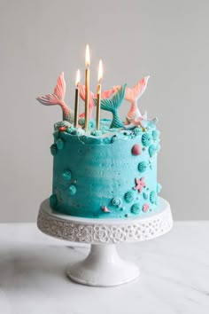 a blue cake with mermaid decorations and candles