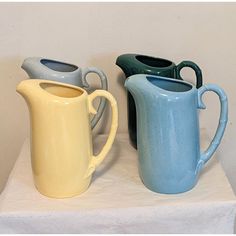 three different colored vases sitting on top of a white tableclothed surface, one is blue and the other is yellow