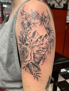 a woman's arm with flowers and mountains on it