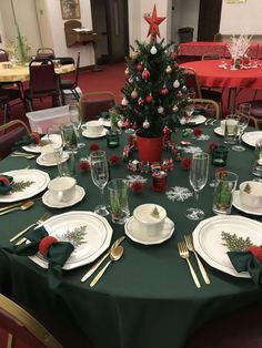 a table set for christmas dinner with plates, silverware and a small tree in the center