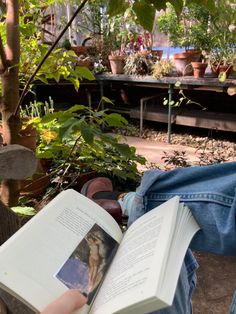 a person laying down reading a book in a garden filled with potted plants and trees