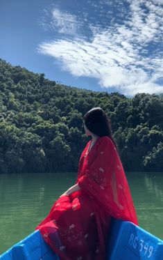 a woman in a red sari is sitting on a blue raft and looking out over the water