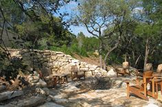 there are many wooden chairs and tables on the stone patio in front of some trees