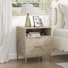 a nightstand with two drawers and a lamp on top of it next to a bed