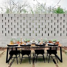 the table is set for four in front of a brick wall with potted plants on it