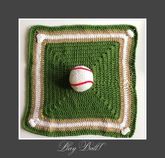 a crocheted square with a ball on it and the words play ball written in white