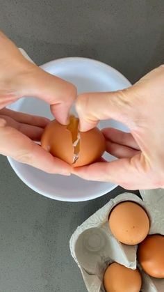 two hands peeling an egg from a white plate on a gray countertop next to eggshells