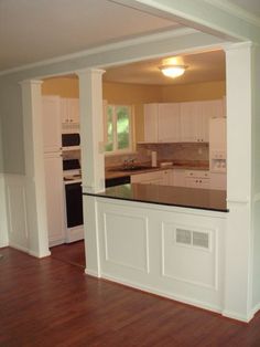 an empty kitchen with white cabinets and black counter tops is seen from the living room