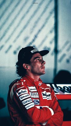 a man in a red racing suit and hat looking off into the distance with his arms crossed