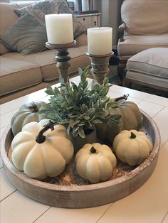 pumpkins and greenery are arranged in a bowl on a coffee table with candles