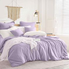 a bed with purple comforter and pillows in a white room next to a window