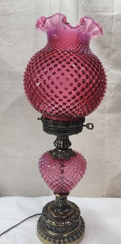 a pink glass vase sitting on top of a metal stand next to a white wall