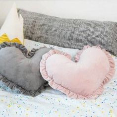 two heart shaped pillows sitting on top of a bed next to a pillow with a ruffle