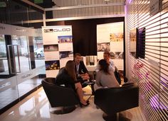 three people sitting in chairs talking to each other at a booth with posters on the wall