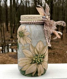 a jar with flowers painted on it sitting on a table in front of some trees