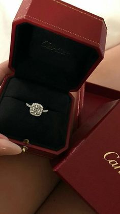 a woman's hand holding an engagement ring in a red box