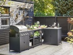 an outdoor kitchen with grill, table and planters on the deck area next to it