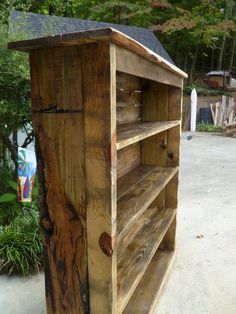 a wooden book shelf sitting in the middle of a yard next to a fence and trees