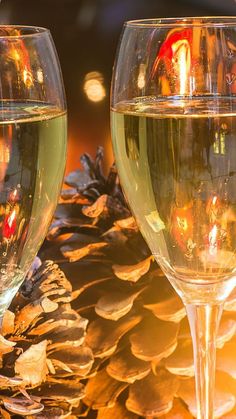 two wine glasses sitting next to each other with pine cones on the table behind them