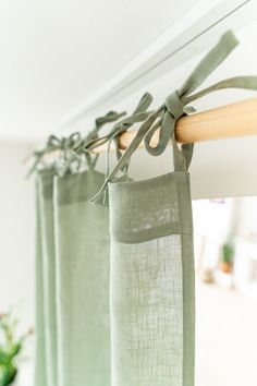 green curtains hanging on a rod in front of a white wall and potted plant