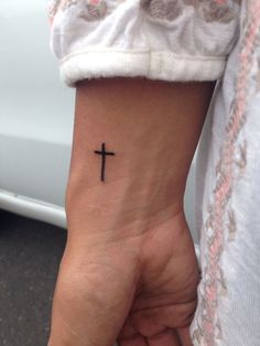 a woman's wrist with a small cross tattoo on the left side of her arm