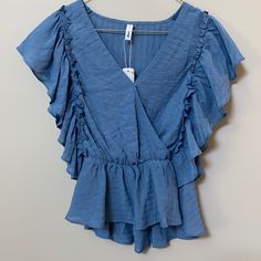 Blue Peplum Top With Surplice Neck (Snap Closure) And Ruffled Sleeve With Elastic Waist. Blue Flutter Sleeve Tops With Ruffle Hem, Blue Tops With Ruffle Hem And Flutter Sleeve, Blue Flowy Tops With Ruffle Sleeves, Blue Flowy Top With Ruffle Sleeves, Flowy Blue Top With Ruffle Sleeves, Blue Ruffle Sleeve Tops For Vacation, Blue Ruffle Hem Top For Beach, Trendy Blue Flowy Blouse, Blue Trendy Loose Fit Tops