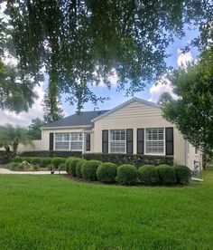 a house that is in the grass with bushes around it and trees on either side