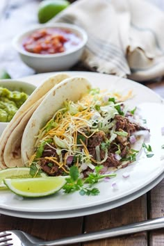 two tacos on a plate with guacamole and salsa in the background