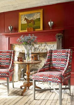 two chairs and a table in front of a fire place with a horse painting on the wall