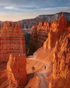 a person walking on a trail in the desert near many large rocks and cliffs with trees