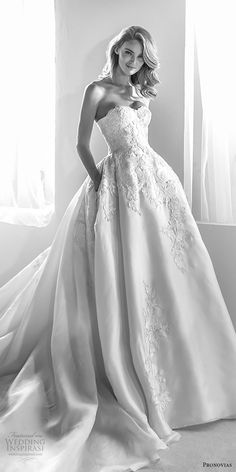 black and white photograph of a woman in a wedding dress standing by a window with her hands on her hips