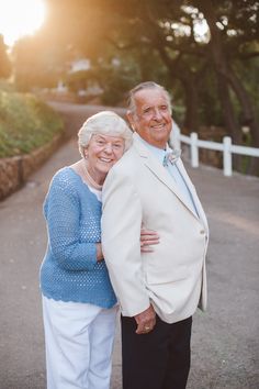 an older man and woman standing next to each other in front of the sun setting