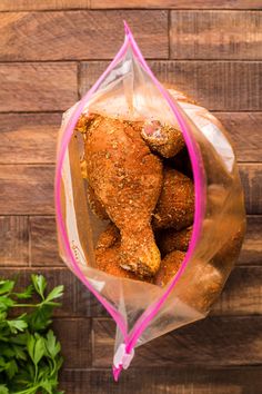 a clear bag filled with chicken wings on top of a wooden table next to a plant