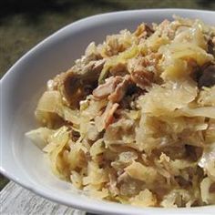 a white bowl filled with cabbage and meat on top of a wooden table next to a bottle