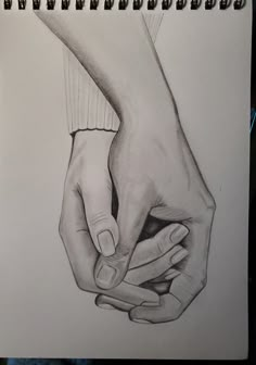 a pencil drawing of two hands holding each other's fingers on a notebook page