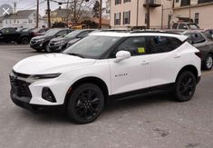 a white chevrolet suv parked in a parking lot next to other cars on the street