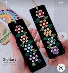 a person holding two black tags with colorful flowers on them and one has a string attached to it