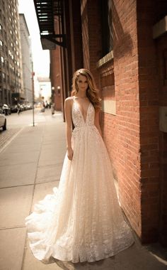 a woman in a wedding dress leaning against a brick wall on the sidewalk next to a building