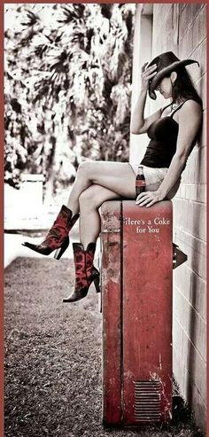 a woman in cowboy boots sitting on top of an old red suitcase with her legs crossed