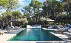 an outdoor pool with lounge chairs and umbrellas next to the swimming pool surrounded by trees