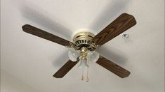 a ceiling fan with three wooden blades and two white flowers hanging from it's center