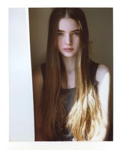 a young woman with long hair standing in front of a white wall and looking at the camera