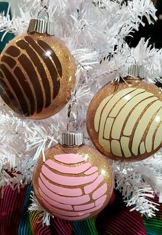 three ornaments are hanging from a white christmas tree with pink and brown designs on them