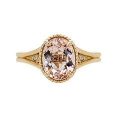 a ring with an oval shaped pink morganite and two diamonds on the band, set in yellow gold