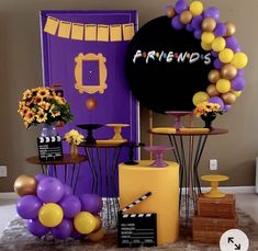 a purple and yellow birthday party with balloons, cake stand, table decorations and sign