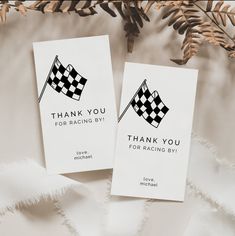 two thank you cards with black and white checkered flags on them next to pine branches